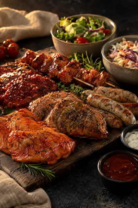 Verschillende soorten vlees, gemarineerd en klaar voor de grill, met sausjes en salades.