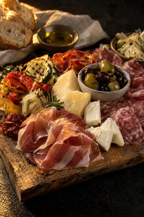 Plank met Italiaanse voorgerechten: vleeswaren, kazen, olijven en gegrilde groenten in olijfolie.